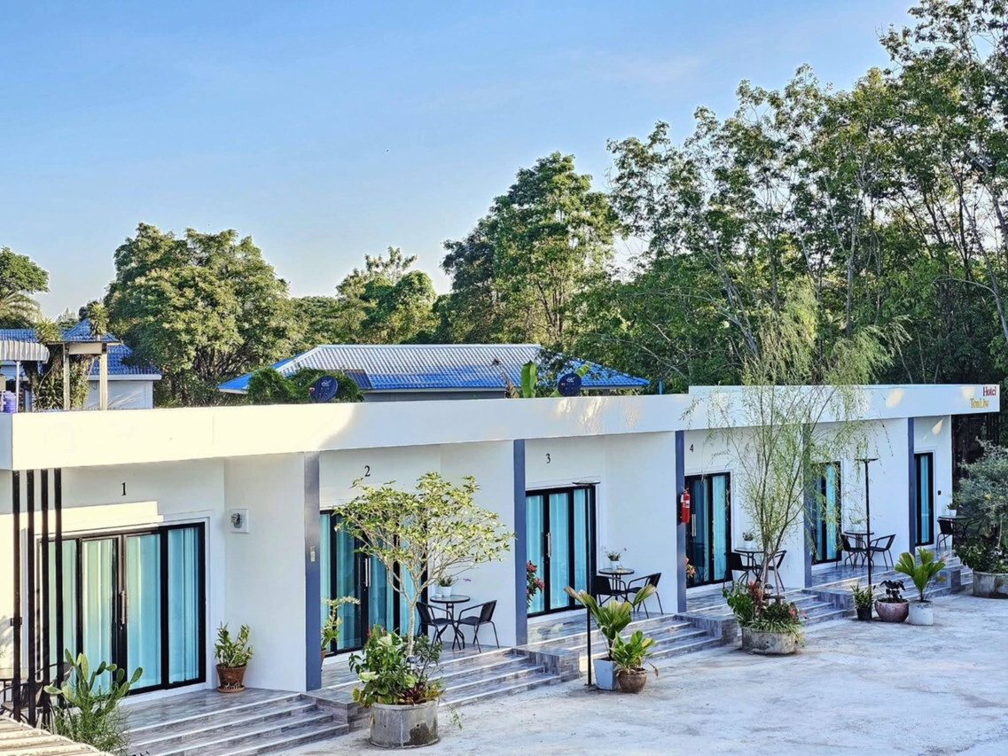 Side view of TonLiw Hotel's white single-storey room block with garden trees