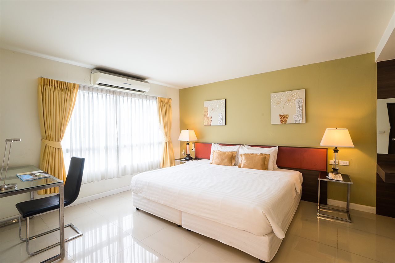 Beyond Suite Hotel guest room with a king bed, olive accent wall and yellow curtains
