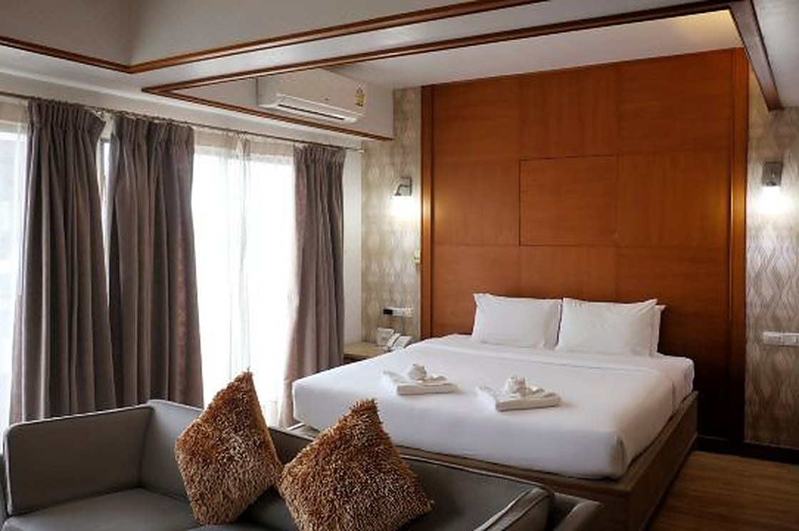 Deluxe room at Nonthaburi Palace Hotel with a large bed, wood-panel wall and balcony