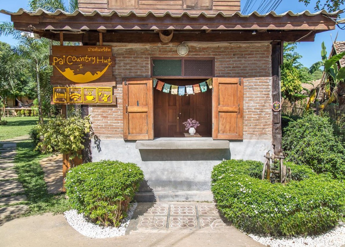ทางเข้าบ้านไม้พร้อมป้าย Pai Country Hut กลางสวน