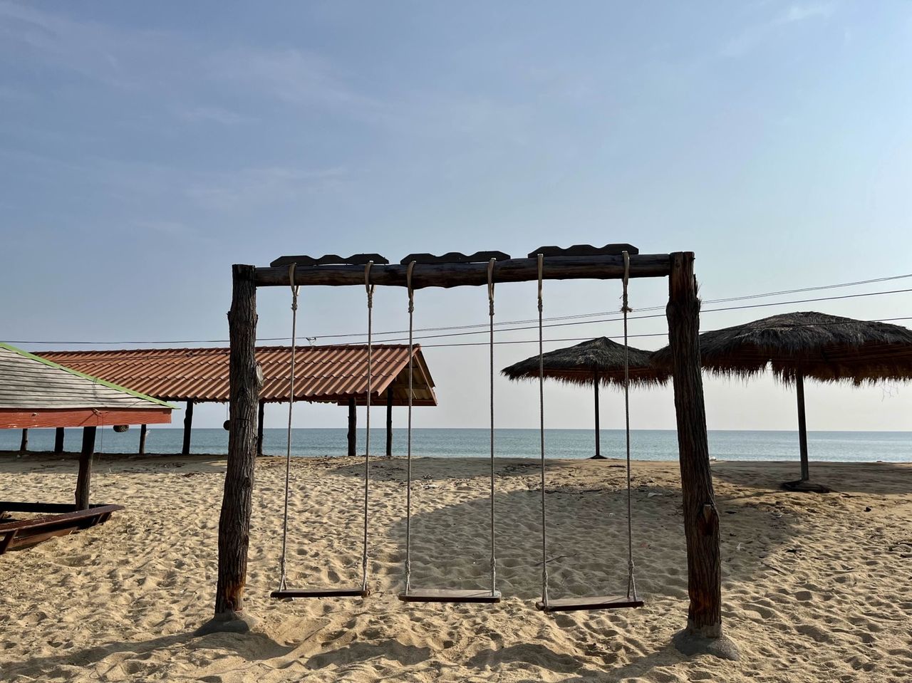 Wooden beach swing and palm-thatch umbrellas by the water, looking out to the Gulf of Thailand