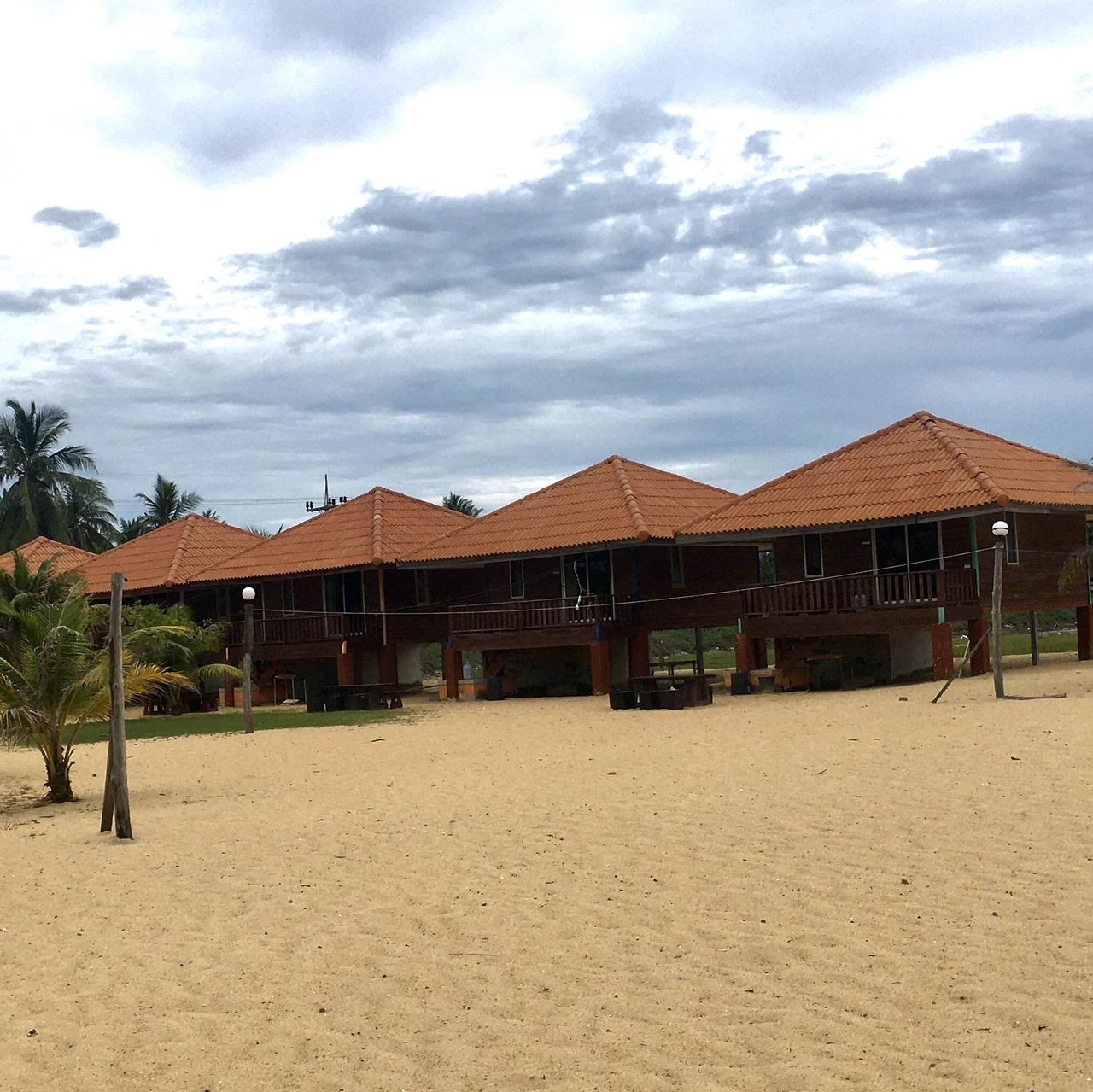 Row of raised wooden bungalows with orange tiled roofs on the sand at the resort