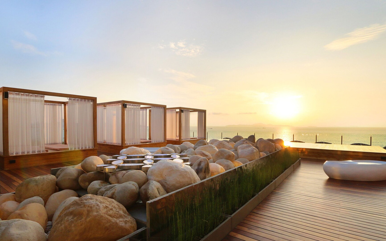 Rooftop deck with cabanas and round-boulder garden facing the sunset over the sea