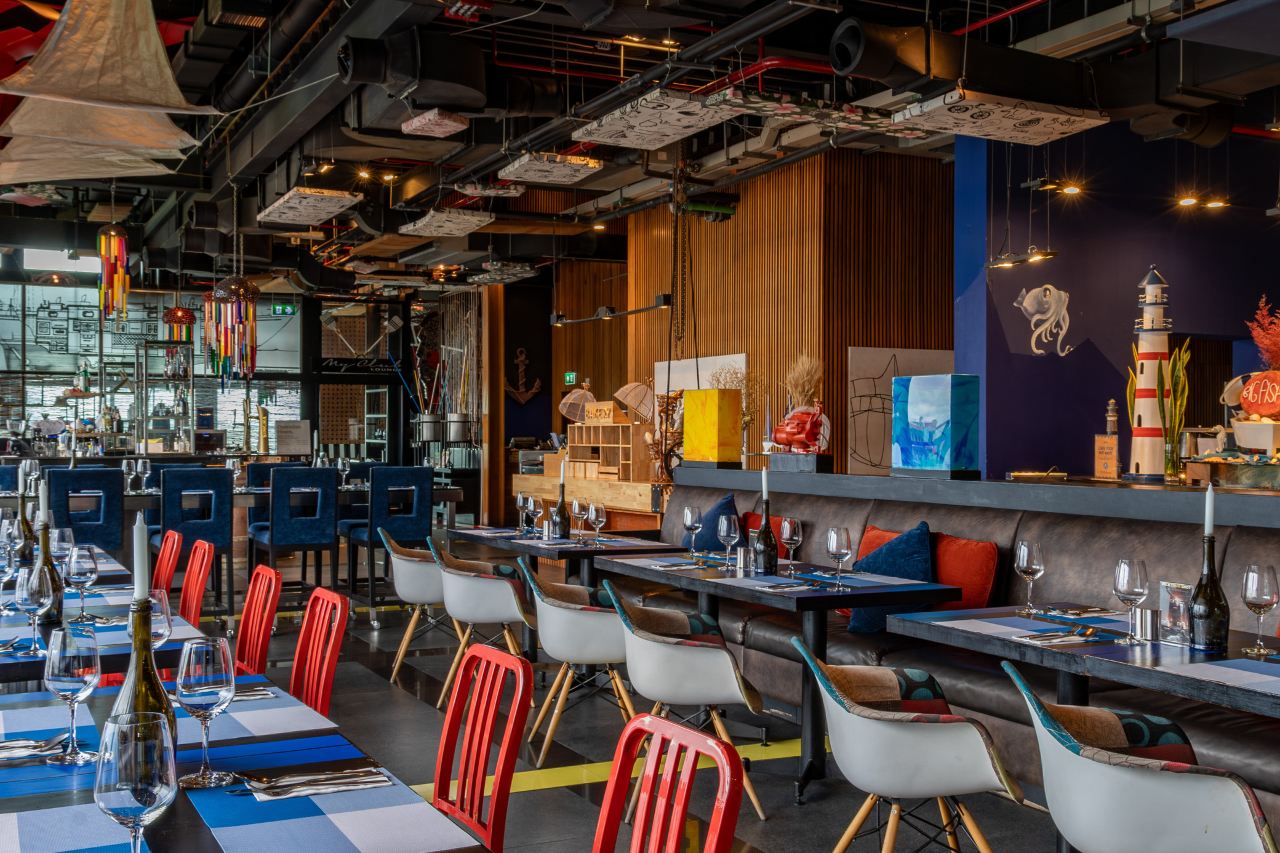 Industrial-loft restaurant with exposed ceiling pipes and colourful chairs