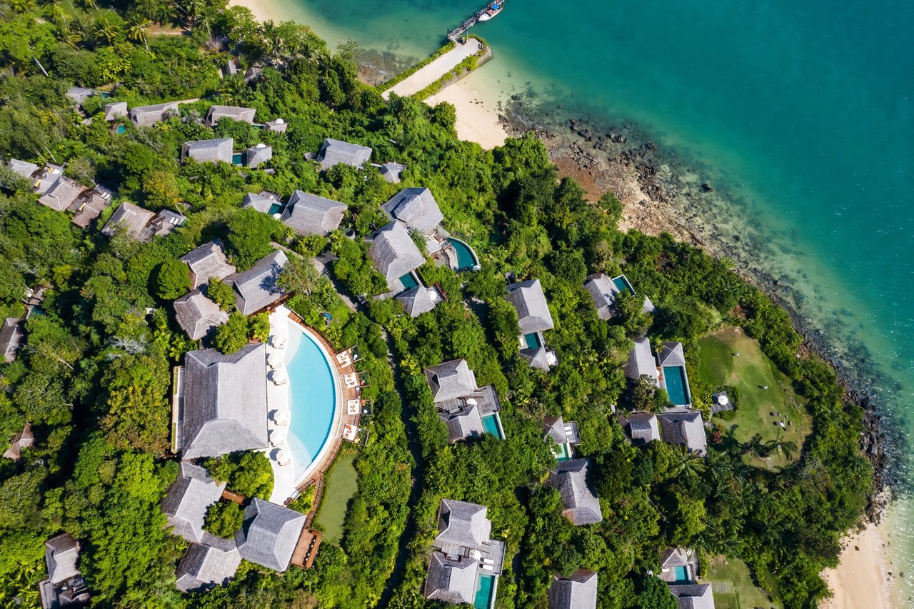 Aerial view of Six Senses Yao Noi thatched-roof villas along the forested hillside above the beach