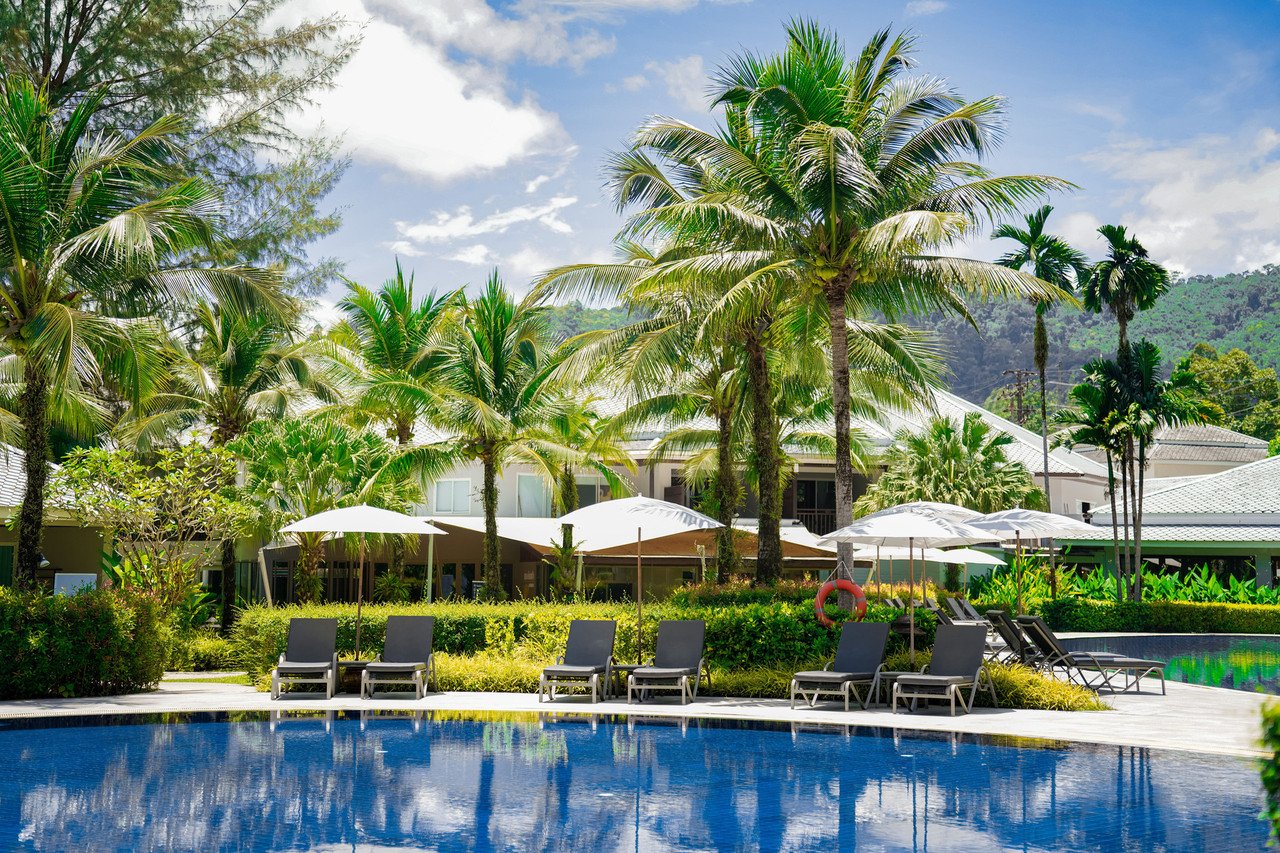 Garden swimming pool among coconut palms with sun loungers and white umbrellas