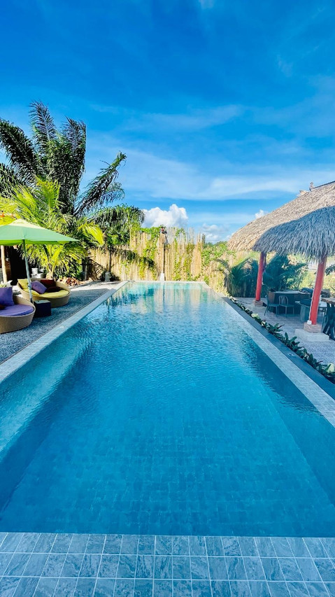 Infinity pool by the canal at Canal Village Pakpra, with garden and thatched salas
