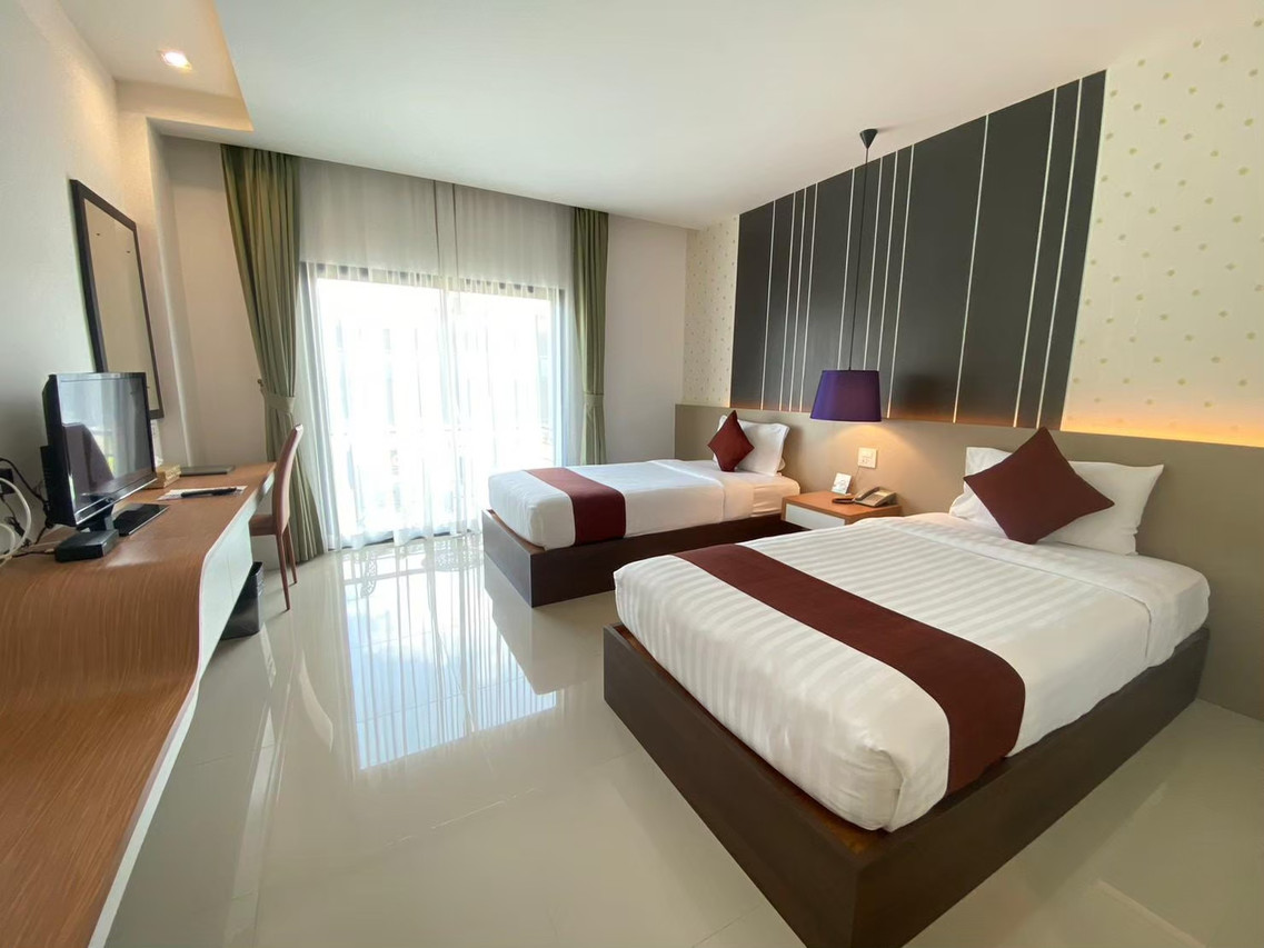Deluxe room at Siva Royal Hotel with twin beds, a dark striped feature wall, glossy floor, work desk and balcony