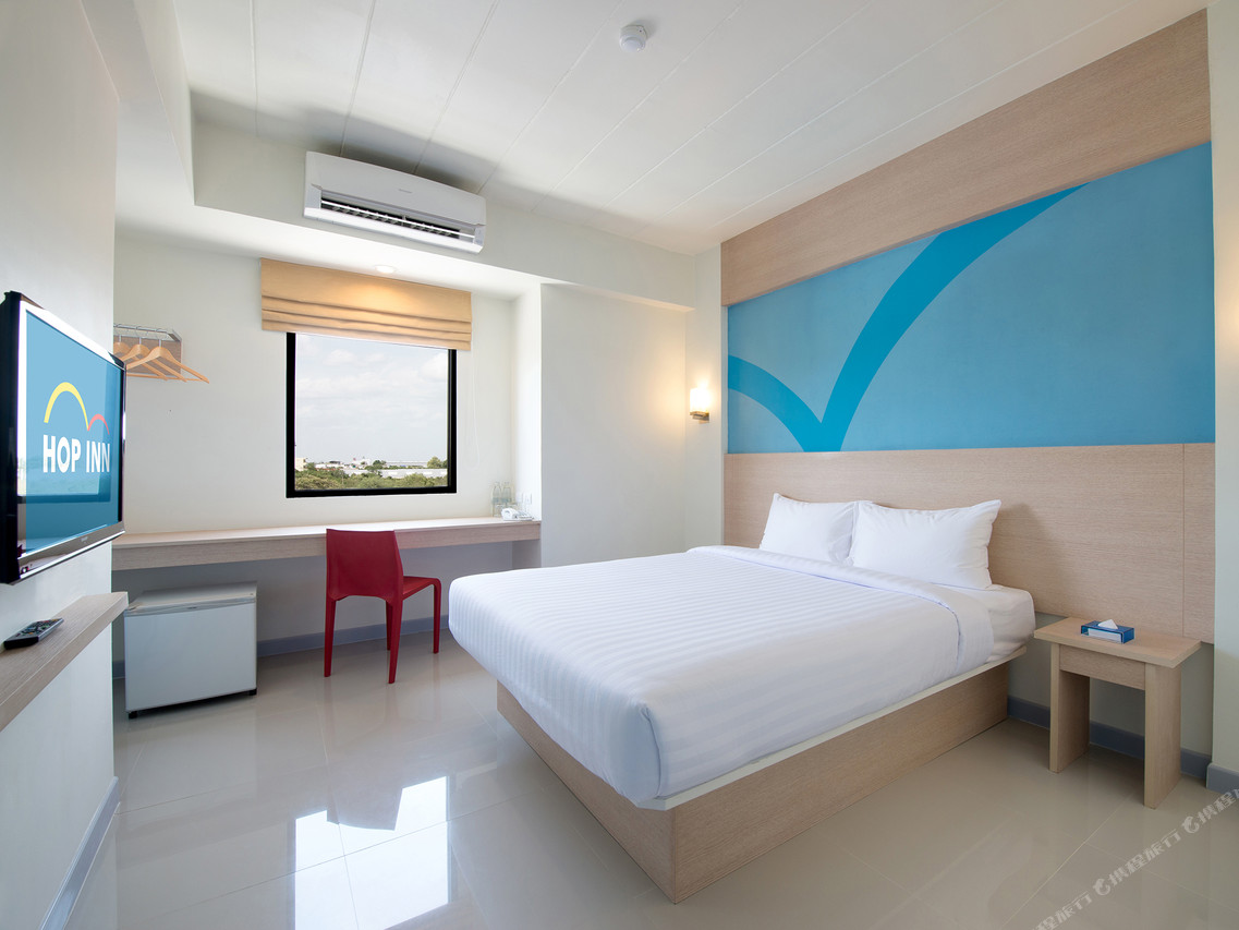 Standard Double room with one large bed, crisp white linens, a red chair, a window desk with a town view and a small fridge underneath