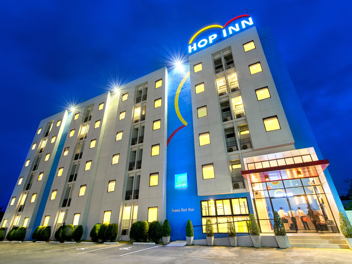 Hop Inn Phetchabun exterior at night with the illuminated HOP INN sign and a glass-fronted lobby, Thai-language hotel signage on the facade