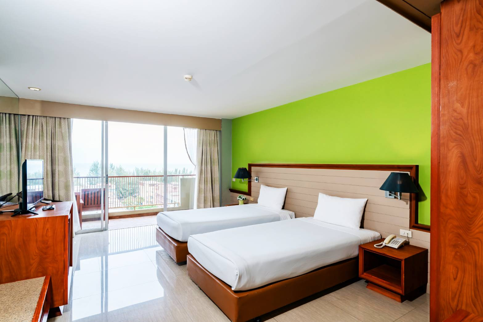 Twin-bed guest room with a green accent wall and a sea-view balcony