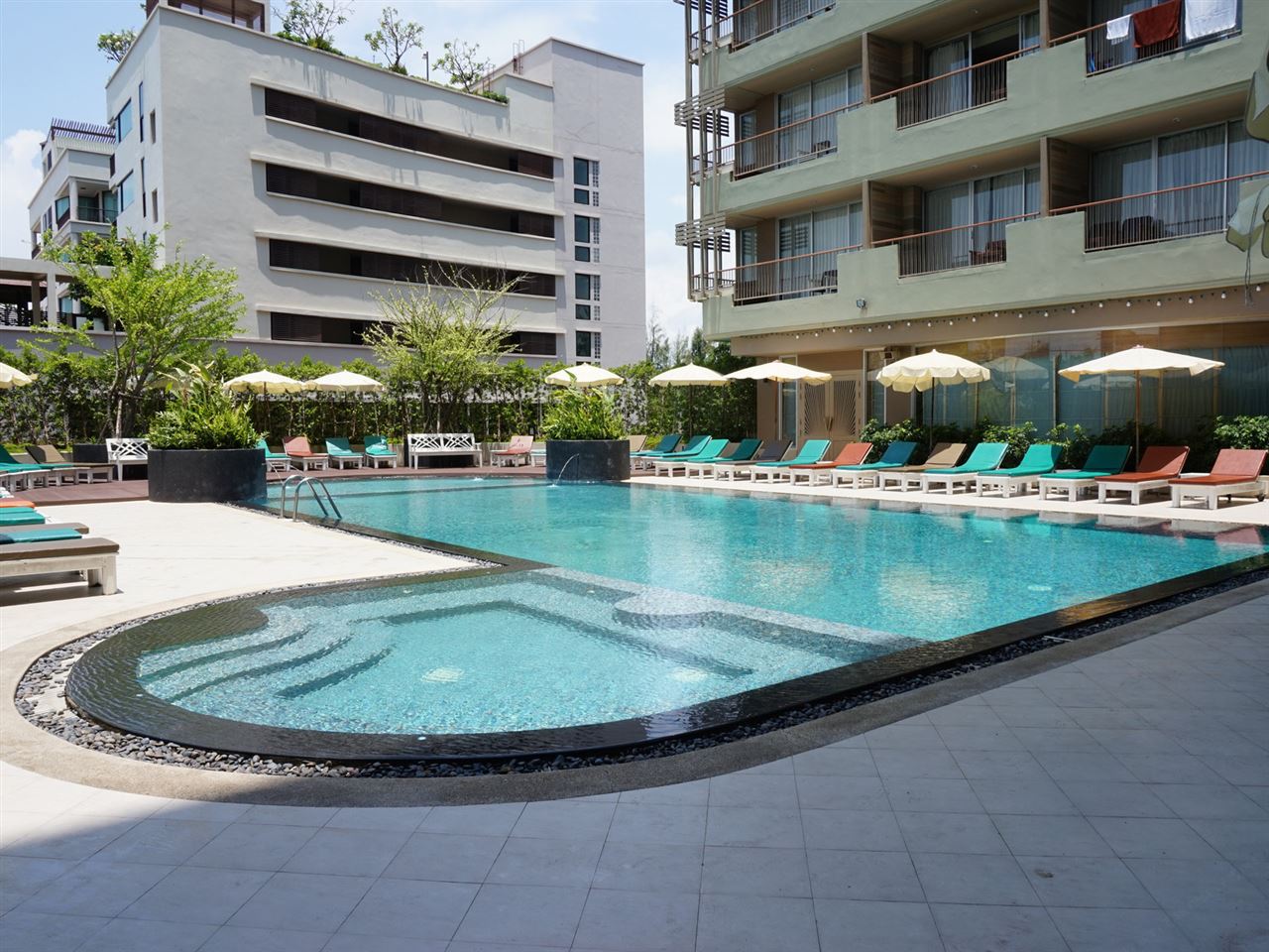 Curved swimming pool with colourful sun loungers near Cha-Am Beach
