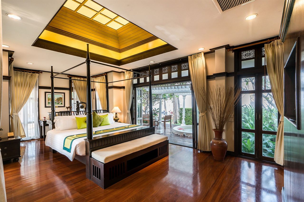 Villa bedroom with a four-poster bed, carved timber ceiling and a garden-and-tub outlook