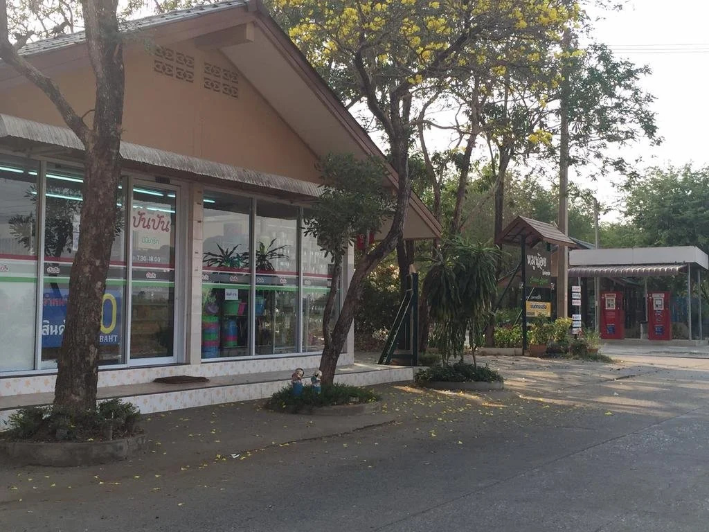 อาคารชั้นเดียวของ Moo Noi Resort พิจิตร มีต้นไม้ใหญ่และร้านสะดวกซื้อในที่