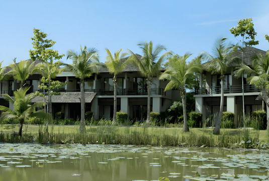 Guest buildings with pitched roofs reflected in the lotus lake across the 20-rai grounds