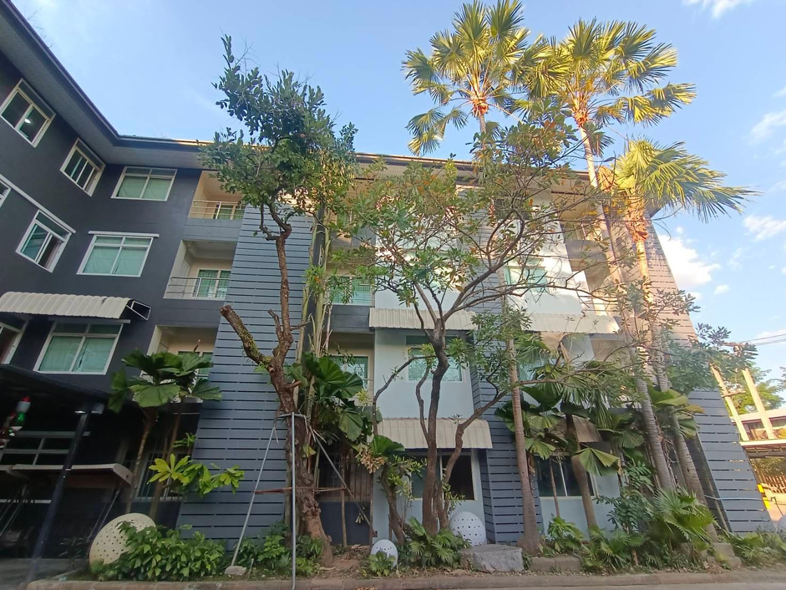 Charcoal-grey exterior of Huan Chetawan hotel with palm trees and a garden