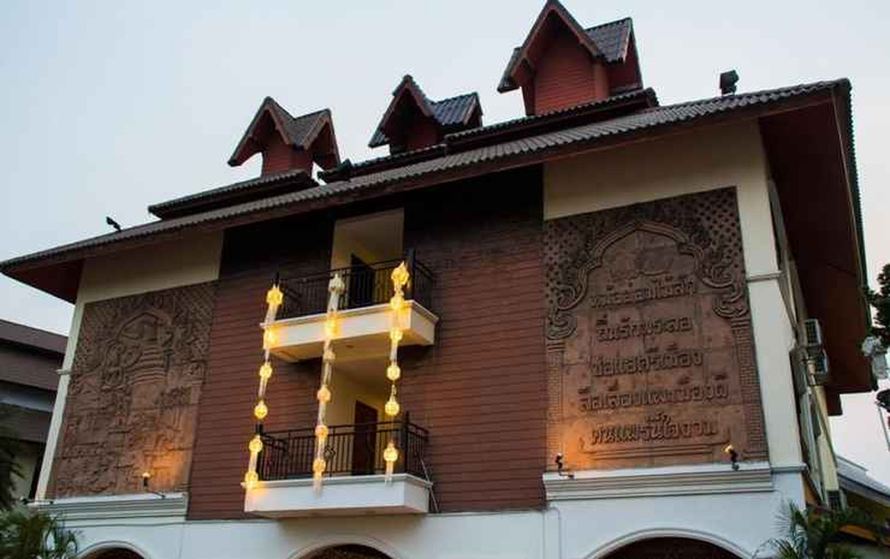 Carved teak Lanna relief on the building facade with a lantern-lit balcony