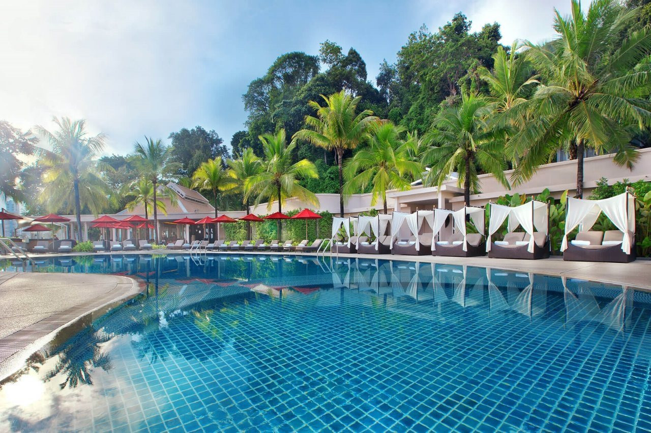 Free-form pool with white daybed cabanas among palm gardens