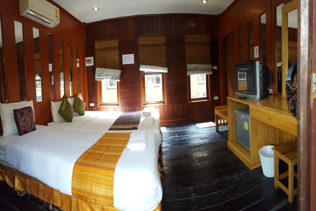 Wide view of a teak cabin room with TV, fridge and dressing table