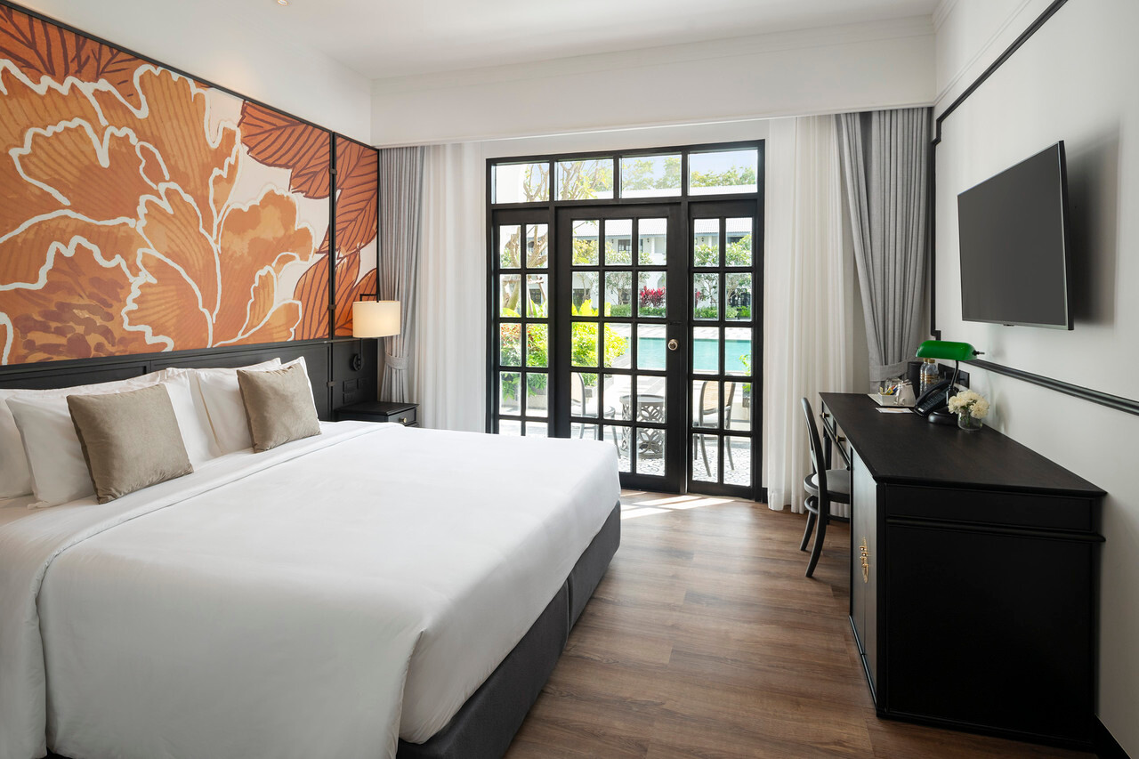 Deluxe room at Indochina Hotel with French doors opening onto the pool and an orange floral headboard