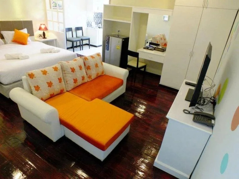 Studio room at Thanasiri Hotel with dark-wood floor, orange sofa bed, kitchenette and fridge