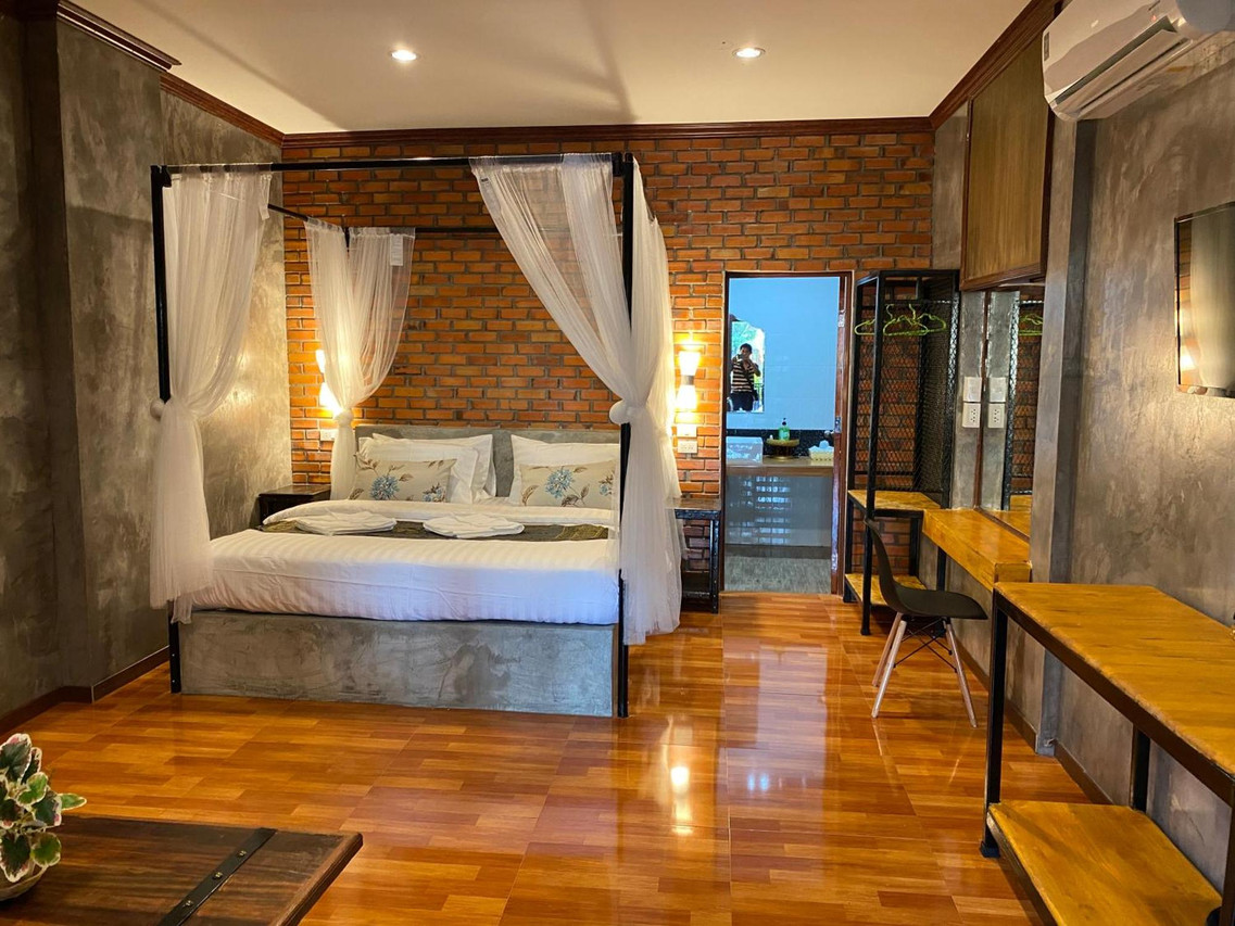 Loft room with exposed brick wall, canopy bed and polished teak floor at Khum Lanna