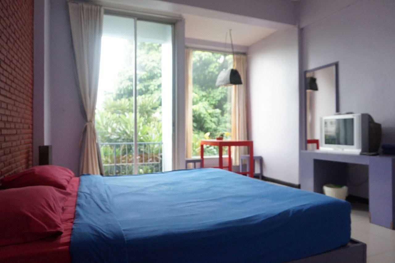 ห้องพัก The SP Hotel ศรีสะเกษ เตียงผ้าปูฟ้า ระเบียงกระจกบานเลื่อนมองเห็นต้นไม้