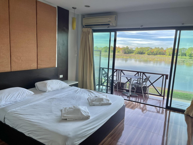 Guest room with a large bed and a balcony overlooking Bueng Chawak lake at Bungchawak Resort