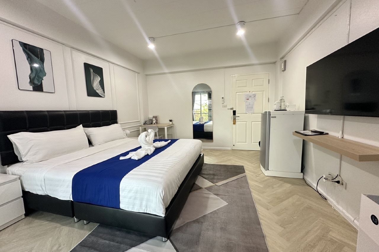 Deluxe King room at The Scene Suphanburi with white walls, black headboard, large TV and refrigerator
