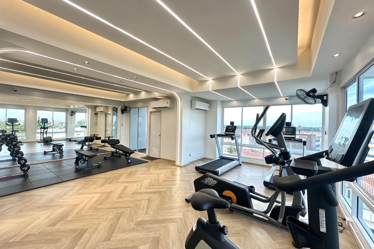 Rooftop gym with treadmills and exercise machines, floor-to-ceiling windows looking over Suphan Buri