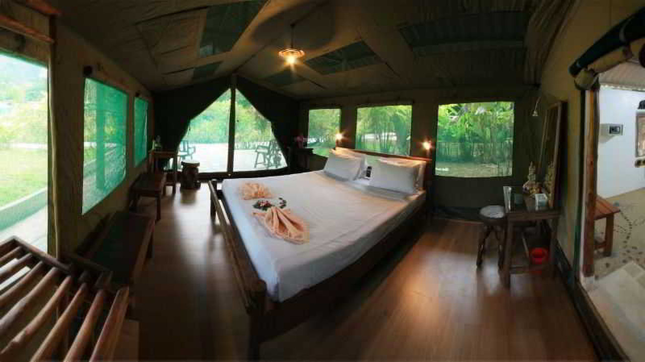 Tent interior with king bed, wooden floors and screened jungle views