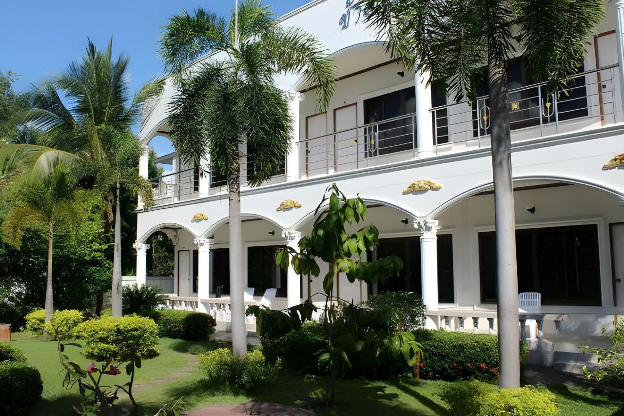 Side view of the white arched building with an upper balcony in the garden at White Elephant Resort Surin