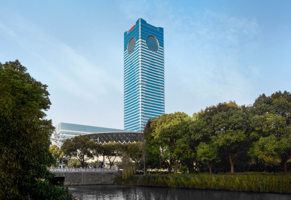 Suzhou Marriott Hotel (苏州万豪酒店) — ตึกแก้วสีน้ำเงินสูงราว 50 ชั้นพร้อมหน้าต่างวงรีคู่ใกล้ยอดและป้าย Marriott ยามพลบค่ำ