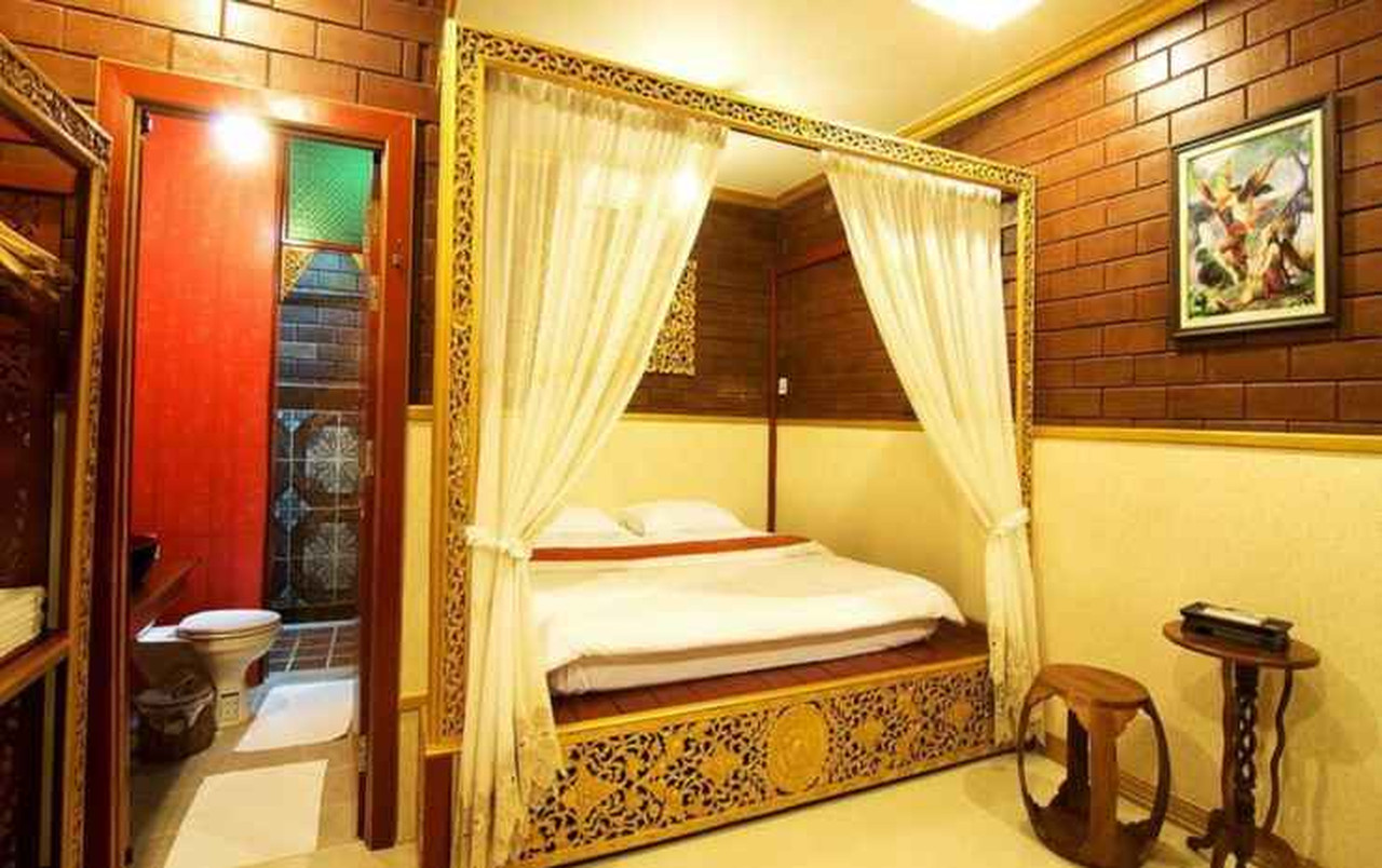 Irawadee Resort guest room with a white-draped four-poster bed, brick walls and en-suite bathroom