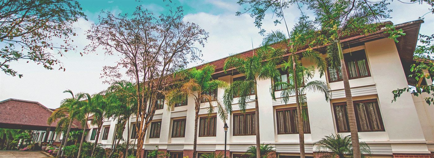 Two-storey white guest building with brick-red roof framed by palms and big trees