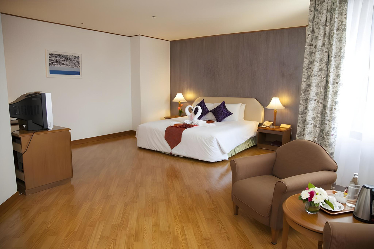 Spacious guest room with wood-look flooring and swan towel art at Thumrin Thana Hotel