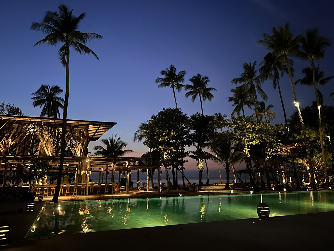 Beachfront pool and bar at The Emerald Cove Koh Chang at dusk, palm trees and the sea behind