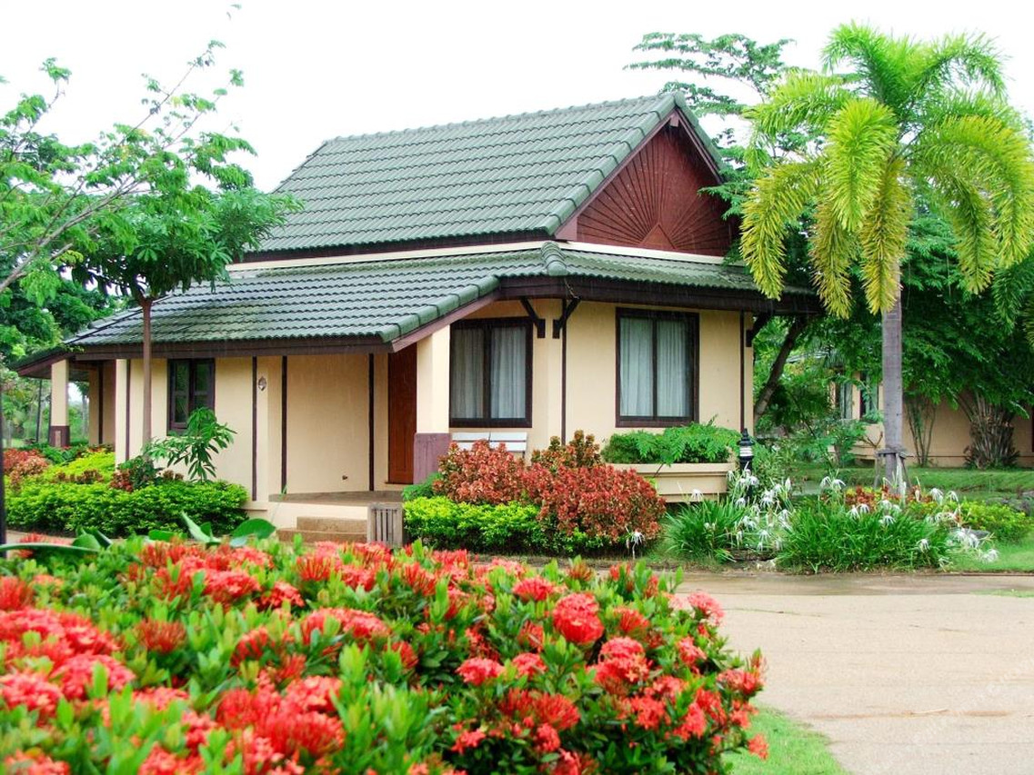 Red ixora flowers and tropical garden in front of a Thai folk-style guest cottage