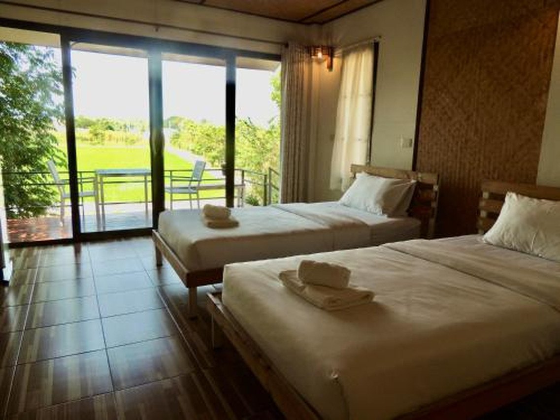 Twin room with a full-height glass wall looking out over rice fields and a wooden balcony