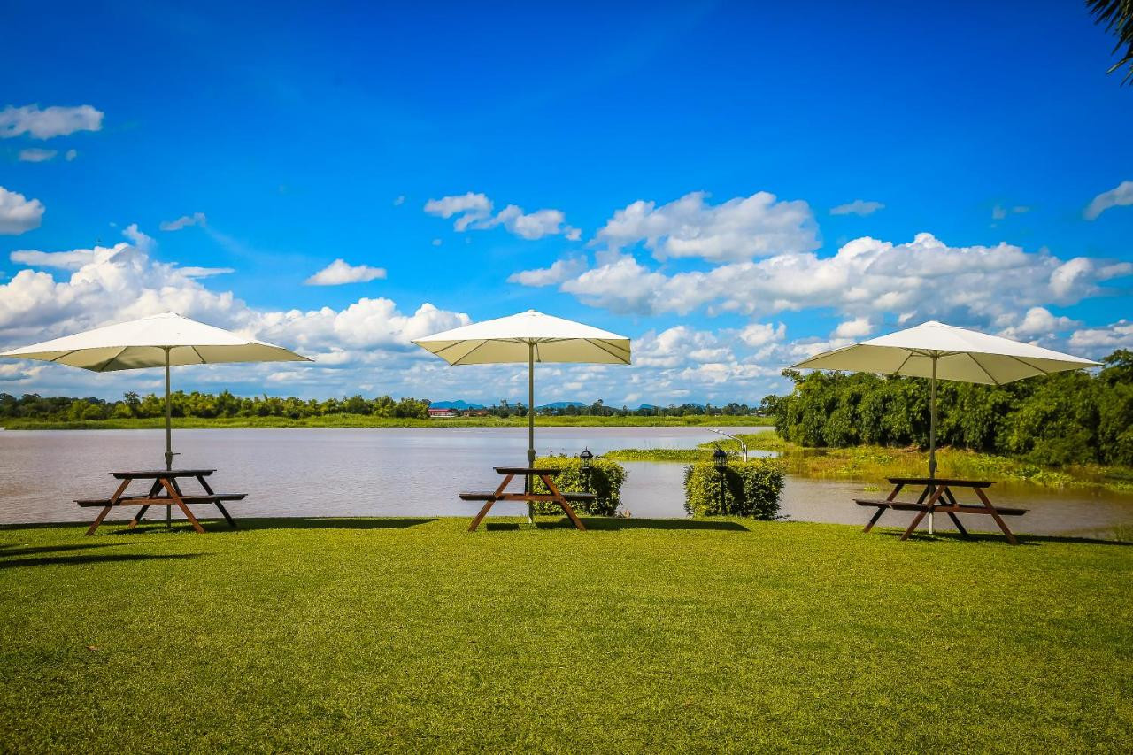 Riverside lawn with white umbrellas and picnic tables facing the Sakae Krang River