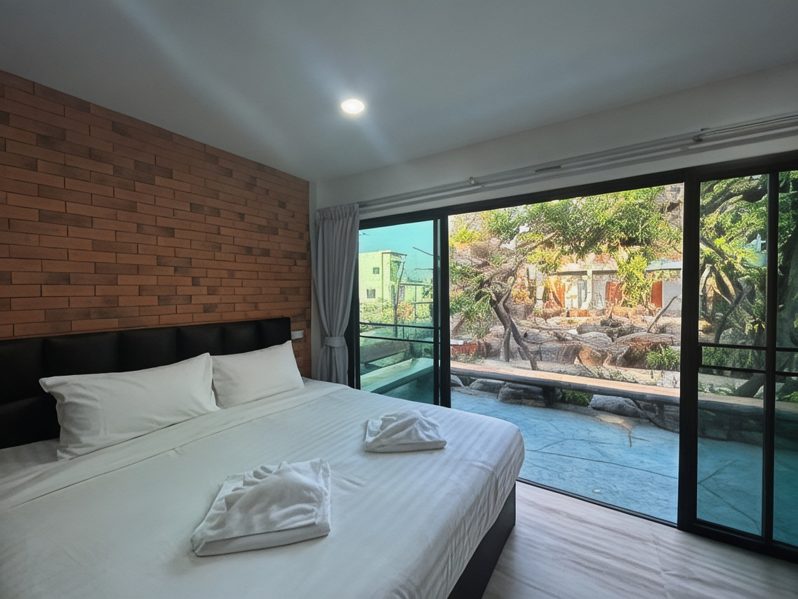 Guest room with an exposed-brick wall, a large bed and sliding glass doors opening to the pool and garden