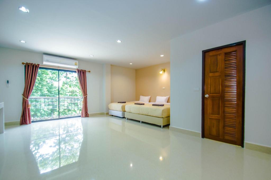 Guest room at Maladee Hotel Uttaradit with white walls and glossy tiled floor, two single beds with brown runners, a sliding glass door to a balcony with greenery outside, and a wooden louvered wardrobe