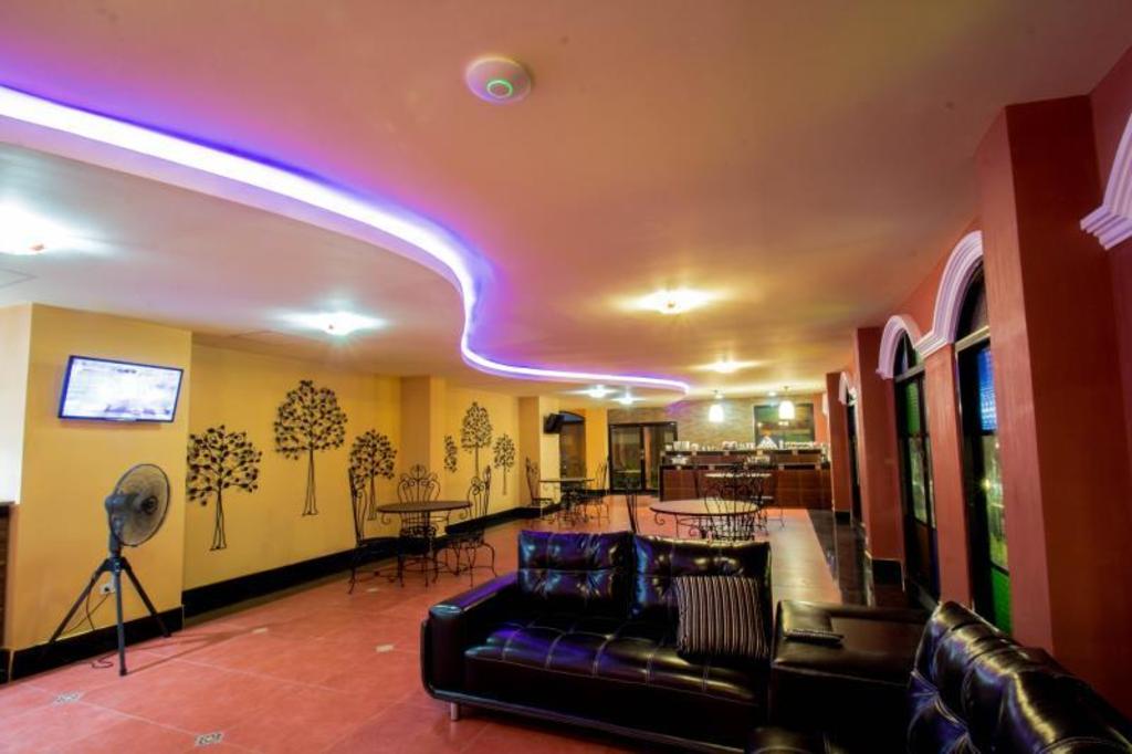 Ground-floor lounge at Maladee Hotel with black leather sofas, wrought-iron tables, tree-motif wall art, purple LED ceiling lighting and a counter at the back