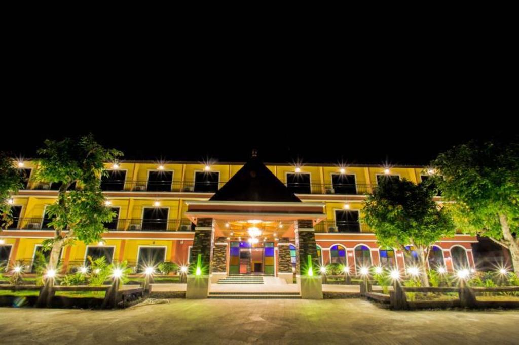 Maladee Hotel building at night, the yellow facade lit up with a pointed-gable entrance porch and lights around the front garden