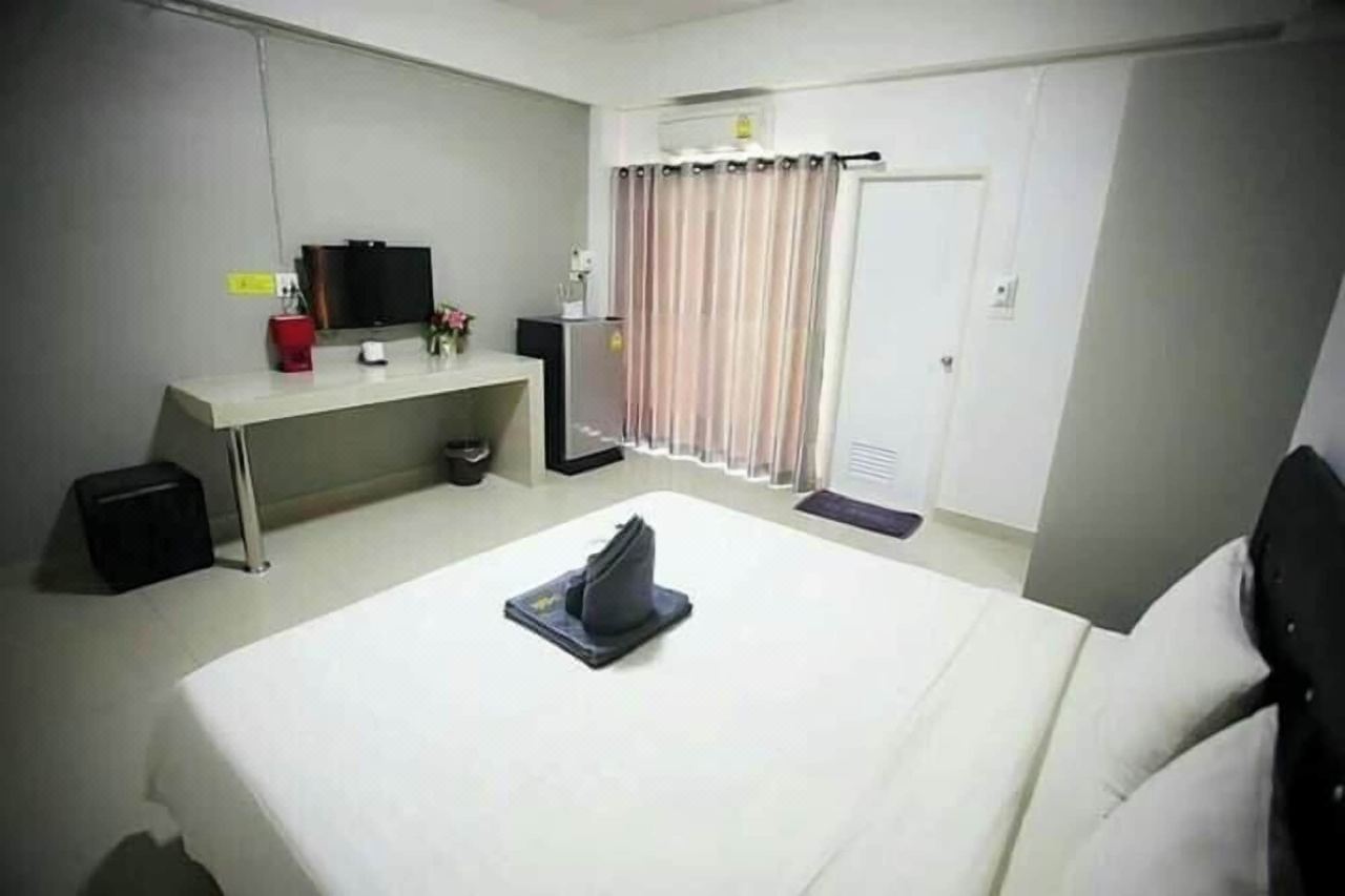 Guestroom with a large bed, desk, TV, fridge and balcony door