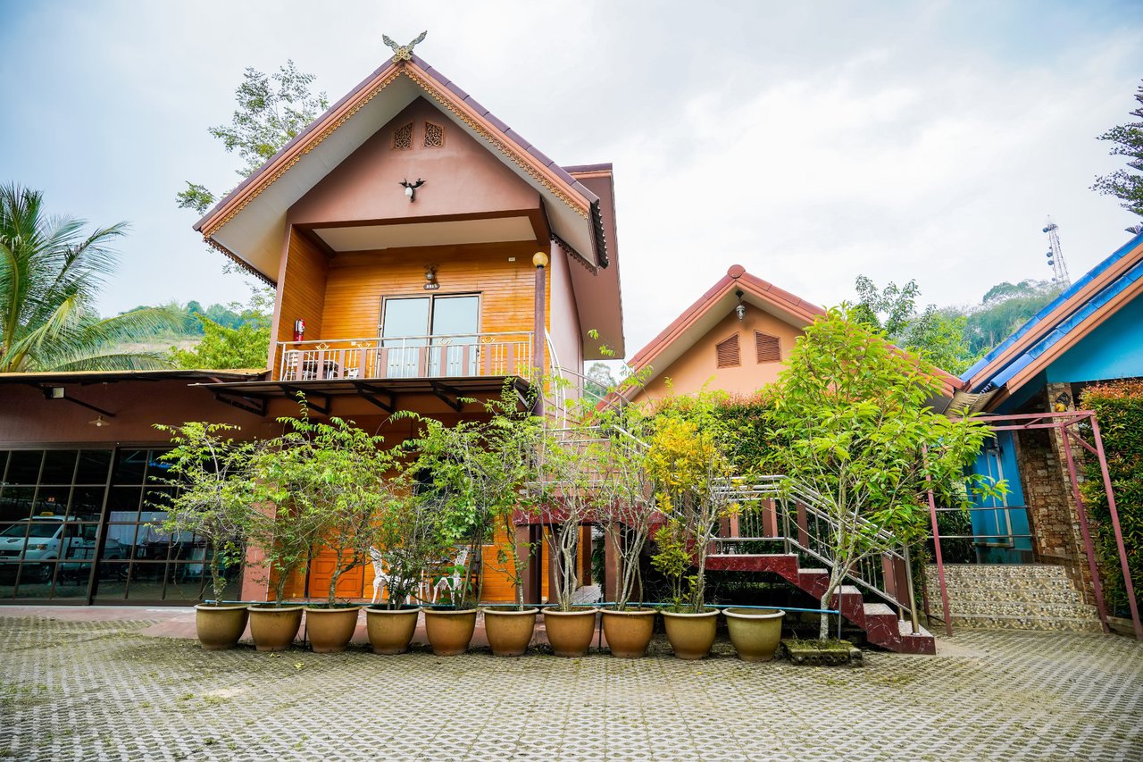 Daytime view of Happy Garden Resort Betong timber chalets with potted plants on a paved courtyard