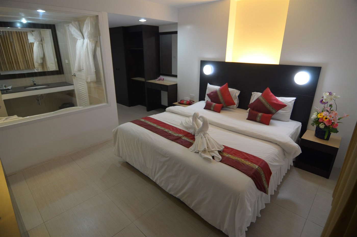 Deluxe room with twin beds, red Thai bed runner and glass-walled bathroom at Modern Thai Hotel Betong