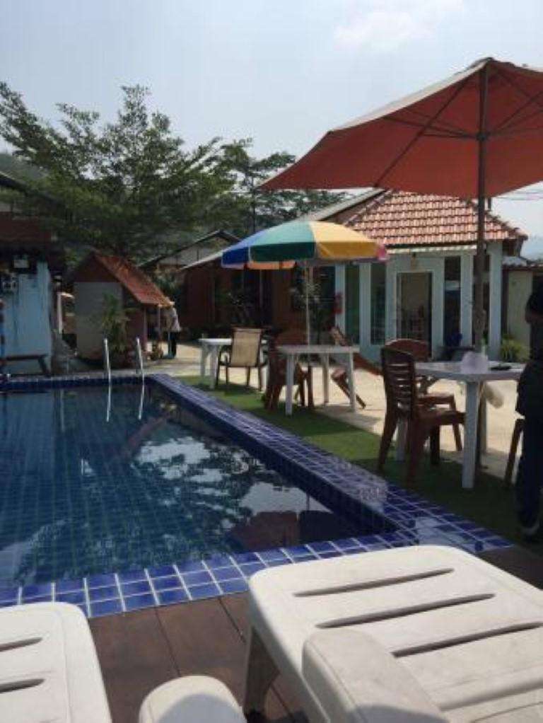 สระว่ายน้ำกลางแจ้งกระเบื้องสีฟ้าของ River Rock Palm Resort มีเก้าอี้อาบแดดและร่มสีส้ม ฉากหลังเป็นเนินเขา