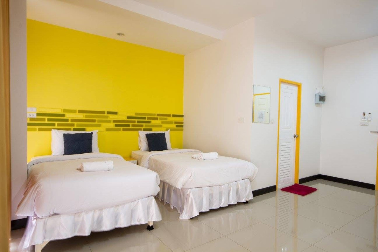 Bright twin room with a yellow accent wall and green-and-yellow tile band, glossy tiled floor at Big Elephant Hotel Yasothon