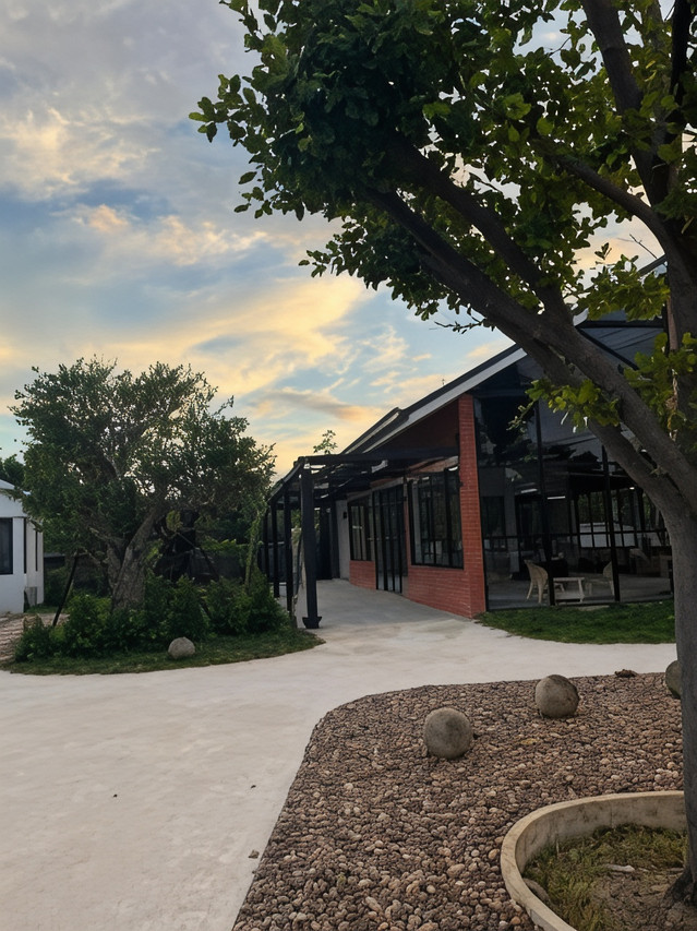 Hotel garden and gravel courtyard at golden hour with a brick-and-glass steel-frame pavilion